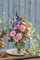 Colourful bouquet of roses (pink), gladioli, fennel blossoms, asparagus, rose hips, autumn anemone, onion blossom in glass vase