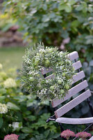 Herb wreath with rosemary, thyme, nigella and meadow chervil tied on a straw bower, hanging on a garden chair