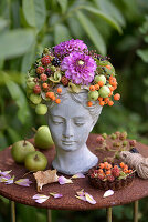 Bust of a woman decorated with berries, ornamental apples and dahlia on garden table