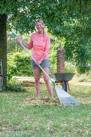 Frau bei Gartenarbeit im Sommer mit Schubkarren und Rechen