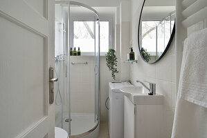 Brightly tiled bathroom with shower cubicle and round mirror