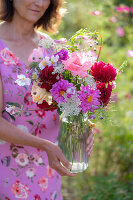 Woman with bouquet of dahlias (Dahlia), roses (Rosa), autumn anemones (Anemone Hupehensis) and wild carrot