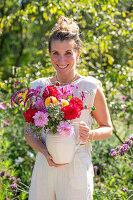 Woman carrying vase with colorful bouquet of dahlias (Dahlia), oriental knotweed (Persicaria orientalis), beard flower (Caryopteris), and borage