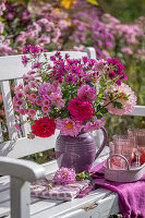 Strauss aus Dahlien (Dahlia), Rosen (Rosa), Astern (Aster) auf Bank vor bunten Blumenbeeten im herbstlichen Garten