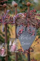 Herz an Gartenzaun hängend mit Wildem Wein und Windlichtern im Herbst