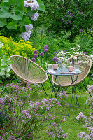 Sitzplatz im Garten mit Sumpf-Wolfsmilch 'Walenburg's Glorie', Zierlauch, Flieder (Syringa), Hortensie (Hydrangea), Schneeflockenstrauch in Blumenbeeten