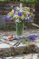 Blumenstrauß aus Rittersporn (Delphinium), Färberkamille (Anthemis tinctoria), Etagenzwiebel, Große Knorpelmöhre, auf Gartenmauer im Bierkrug