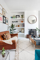 Living room with plants, leather sofa, round mirror and wood-burning stove