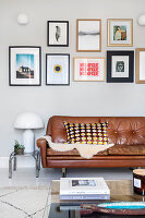 Picture wall above brown leather sofa with patterned cushions and stack of books on glass table