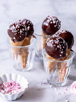 Cake pops with chocolate coating and sprinkles in waffle cones