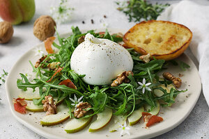 A plate with sliced pears, topped with rocket salad, burrata cheese, roasted walnuts and dried Serrano ham.