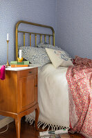 Brass bed and vintage bedside table in bedroom with blue wallpaper with scattered flowers