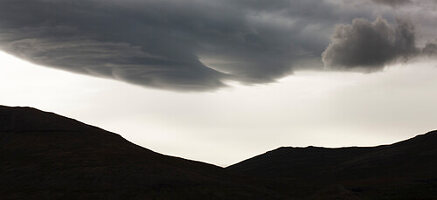 Silhouetted mountain range and large dark cloud