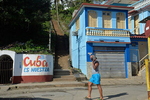Kuba, Baracoa, ein Mann geht auf einer Straße, auf der ein großes Schild mit der Aufschrift "Cuba es nuestra" steht