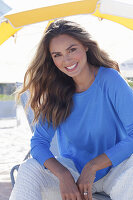 Frau in blauem Pullover und weißer Hose am Strand sitzend