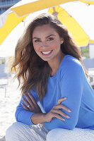Frau in blauem Pullover und weißer Hose am Strand sitzend