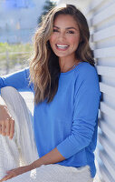 Woman in blue jumper and white trousers sitting on veranda