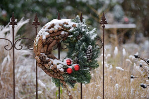 Winterkranz aus Zapfen und Tannengrün an Metallzaun im verschneiten Garten