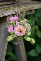 Kleiner Herbststrauß mit Dahlien (Dahlia) und Hopfen (Humulus) in Glasvase an Holzwand