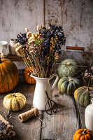 Getrocknete Blumen in weißer Vase auf Holztisch mit Kürbissen und Bastelmaterial, Herbstdeko