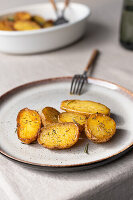 A close-up shot of golden brown roasted potatoes seasoned with herbs on a speckled ceramic plate with a fork on the side.