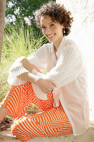 Brunette woman in cream-coloured blouse and orange-coloured patterned trousers