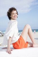 Brunette woman in cream-coloured blouse and orange shorts