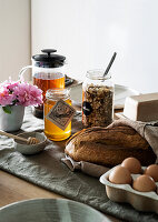 Frühstückstisch mit frischem Brot, Eiern, Honig, Müslimischung und Tee