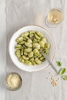 Portion of potato gnocchi with basil â€˜Pestoâ€™ sauce, on light gray background.