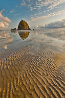 USA, Oregon, Cannon Beach. Sunset golden colors with ripples in sandy beach and The Haystack Rock