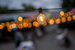 Nahaufnahme einer warm leuchtenden Lichterkette bei einer Hochzeitsfeier im Freien in Malaga,Spanien. Der Bokeh-Effekt sorgt für eine verträumte und romantische Atmosphäre.