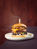 Ein köstlicher Cheeseburger mit knusprigem Speck, geschmolzenem Cheddar-Käse, frischem Salat, roten Zwiebeln, Mayonnaise und Cheddar-Sauce auf einem weichen Brötchen, bereit zum Genuss