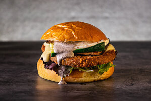 Ein köstlicher veganer Gourmet-Burger mit knusprigen Zucchini, geschmolzenem Käse, frischem Salat und cremiger Soße, serviert auf einem getoasteten Brötchen. Perfekt für Food-Enthusiasten und Burger-Liebhaber.