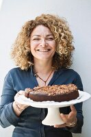 Frau hält einen Tortenständer mit Schokoladekuchen