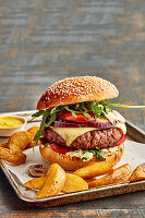 Selbstgemachter Cheeseburger vom Grill mit Rucola und Kartoffelspalten