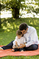 Father and daughter (2-3 years) reading a book, English Garden, Munich, Bavaria, Germay