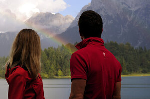 Young couple watching rainbow, lake Lautersee, Mittenwald, Werdenfelser Land, Upper Bavaria, Germany