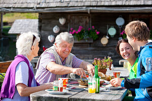 Vier Wanderer beim Essen vor einer Almhütte, Steiermark, Österreich