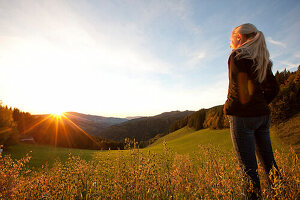 Junge Frau betrachtet Sonnenaufgang auf einer Alm, Steiermark, Österreich