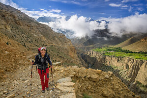 Junge Frau, Wanderer, Trekker in surrealer Landschaft typisch fuer das Mustang in der Hochwueste um das Kali Gandaki Tal, dem tiefsten Tal der Welt. Fruchtbare Felder gibt es in der Hochwueste nur durch ein ausgekluegeltes Bewaesserungssystem. Im Hintergr