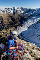 Kletterin blickt am Standplatz in das leicht verschneite, hochalpine Gelände der Zillertaler Alpen, Gigalitz, Tirol, Österreich