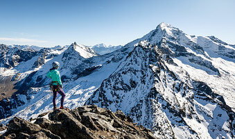 Young woman stands at the summit of the Gigalitz and looks at the high alpine landscape of the Großer Löffler, Zillertal Alps, Tyrol, Austria, which is lightly snowed in autumn