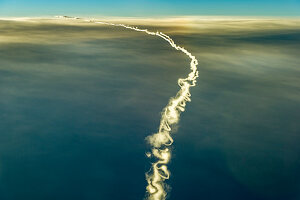 Flugzeug mit langen, dünnen und verwirbelten Kondensstreifen über Wolkenschicht in einer Linkskurve