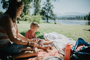 Mother is sitting by the lake with her son on a beautiful summer day and eating an ice cream. Family, summer day, sunshine, lake, Allgäu, Bavaria