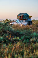 Albania, Southern Europe, young man looks out of the roof tent on an off-road vehicle