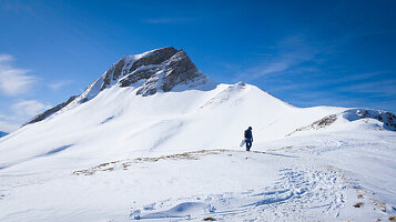 Person mit Splitboard läuft auf Bergrücken vor einem Berggipfel in Damüls im Winter im Schnee