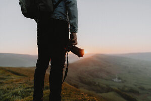 Male photographer with SLR camera on hill overlooking tranquil landscape at sunrise, England