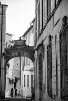 Two women walking through a arched stone gate in the medieval city of Arles, France