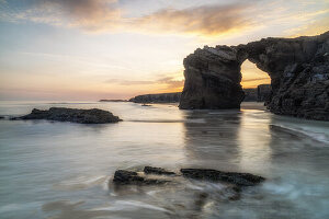 Blick durch einen Felsbogen am Sandstrand von Playa de las Catedralas bei Sonnenuntergang, Gemeinde Ribadeo, Provinz Lugo, Galicien, Nordspanien, Spanien