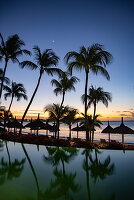  Reflection of coconut palms and thatched umbrellas in the swimming pool of Royal Palms Beachcomber Luxury (Beachcomber Resorts) at dusk, Grand Baie, Rivière du Rempart, Mauritius, Indian Ocean 